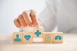 © sorapop - Captured in an image, Hand clutches wooden block featuring healthcare and medical icons. Reflects safety, health, and family well-being, symbolizing pharmacy and heart care. health care concept