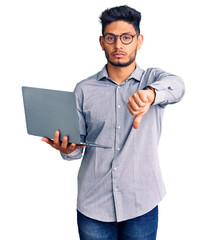 Wall Mural - Handsome latin american young man working using computer laptop with angry face, negative sign showing dislike with thumbs down, rejection concept