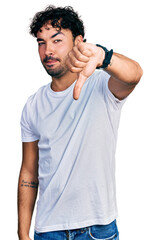 Poster - Hispanic young man with beard wearing casual white t shirt looking unhappy and angry showing rejection and negative with thumbs down gesture. bad expression.