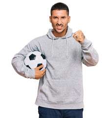 Canvas Print - Handsome man with tattoos holding soccer ball annoyed and frustrated shouting with anger, yelling crazy with anger and hand raised