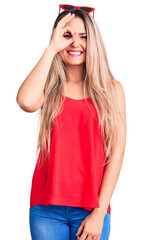 Wall Mural - Young beautiful blonde woman wearing sleeveless t-shirt and sunglasses doing ok gesture with hand smiling, eye looking through fingers with happy face.