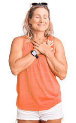 Wall Mural - Middle age fit blonde woman wearing casual summer clothes and sunglasses smiling with hands on chest with closed eyes and grateful gesture on face. health concept.