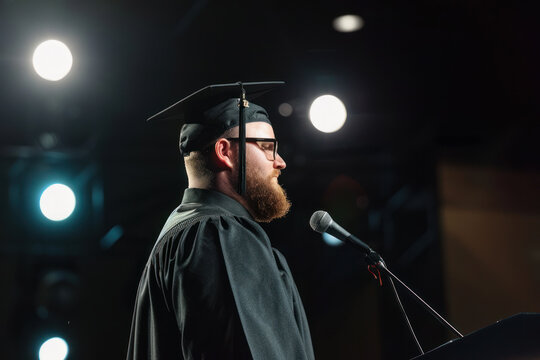 Graduate in a gown and cap with a tassel gives a speech on stage.