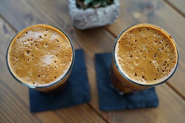 Wall Mural - Top view of two glasses of iced cold frappes on a wooden table