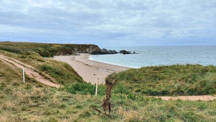 Scenic shot of a grassy hill overlooking the coastline under a cloudy sky