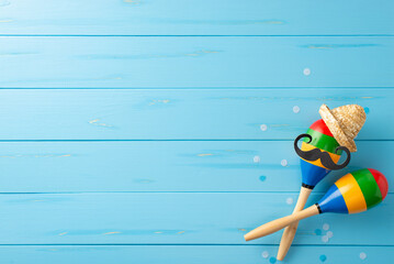 Wall Mural - Cinco de Mayo ambiance captured from top view. Colorful elements like maracas with funny sombrero and mustache arranged on blue wooden background. Ideal for festive promotions