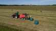 Schwarzer Treker oder Traktor mit einer roten Stroh Festkammerpresse bei der Strohernte auf einem gemähten Feld