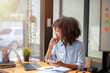 © Wasana - African American woman sitting in front of a laptop and holding a mobile phone