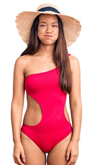 Wall Mural - Young beautiful latin girl wearing swimwear and summer hat puffing cheeks with funny face. mouth inflated with air, crazy expression.