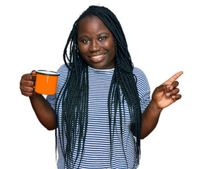 Wall Mural - Young black woman with braids drinking a cup coffee smiling happy pointing with hand and finger to the side