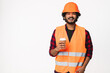 Happy young Indian construction worker in orange uniform and helmet drinking coffee isolated over white background. Hindi engineer builder drinking hot beverage