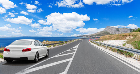 Wall Mural - A white car drives along the sea coastline on a sunny summer day.