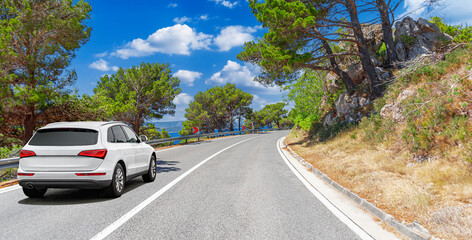 Wall Mural - A white car drives along the sea coastline on a sunny summer day.