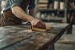 A close-up image capturing the precise moment an artisan's hand moves a sanding block across the rich, textured grain of a wooden surface. 
