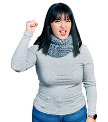 Poster - Young hispanic plus size woman wearing winter scarf angry and mad raising fist frustrated and furious while shouting with anger. rage and aggressive concept.