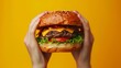 Hands holding a burger, yellow background