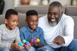 Grandfather laughs with grandsons, holding multicolored eggs, joyous bond in home's comfort. Elderly man shares chuckles with two boys, vibrant spheres in hand, radiating familial happiness.
