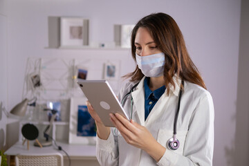 A female doctor in a mask and white uniform uses a tablet in her work. Technologies