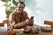 Indian man wearing traditional cloth uses smartphone while waiting for food, smile at camera, Indian food