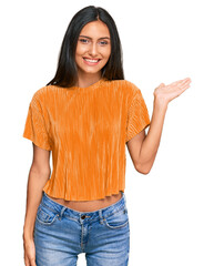 Sticker - Young brunette arab woman wearing casual clothes smiling cheerful presenting and pointing with palm of hand looking at the camera.