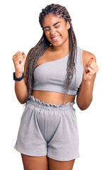 Canvas Print - Young african american woman with braids wearing sportswear very happy and excited doing winner gesture with arms raised, smiling and screaming for success. celebration concept.