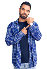 Sticker - Young hispanic man wearing casual clothes in hurry pointing to watch time, impatience, looking at the camera with relaxed expression