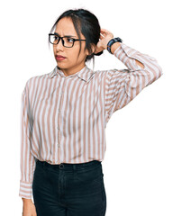 Wall Mural - Young hispanic girl wearing casual clothes and glasses confuse and wondering about question. uncertain with doubt, thinking with hand on head. pensive concept.