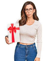 Canvas Print - Young brunette woman holding gift thinking attitude and sober expression looking self confident