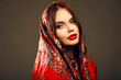 Russian girl Matryoshka style. Fashion woman portrait with traditional red headscarf. Beauty girl model with red lips makeup isolated on studio background.