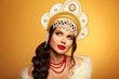 Beautiful brunette woman portrait in fur coat and kokoshnik (woman's headdress in old Russia). Pretty model girl with red lips and plait hairstyle isolated on grey studio background.