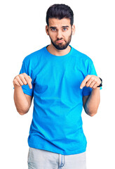 Wall Mural - Young handsome man with beard wearing casual t-shirt pointing down looking sad and upset, indicating direction with fingers, unhappy and depressed.