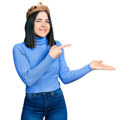 Poster - Young brunette woman with blue eyes wearing princess crown amazed and smiling to the camera while presenting with hand and pointing with finger.