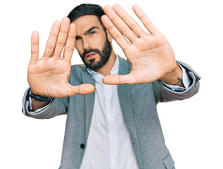 Wall Mural - Young hispanic man wearing business clothes doing frame using hands palms and fingers, camera perspective