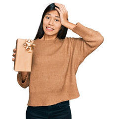 Canvas Print - Beautiful young asian woman holding gift stressed and frustrated with hand on head, surprised and angry face