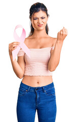 Poster - Young beautiful woman holding cancer awareness pink ribbon annoyed and frustrated shouting with anger, yelling crazy with anger and hand raised