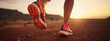 Lady or female / woman South-African trail runner running on a red stadium track with a close-up of the trail running shoes during sunset 