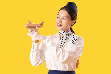 Canvas Print - Beautiful Asian stewardess with wooden airplane on yellow background