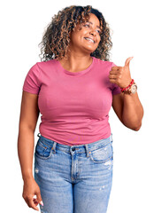 Wall Mural - Young african american plus size woman wearing casual clothes smiling with happy face looking and pointing to the side with thumb up.