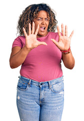 Wall Mural - Young african american plus size woman wearing casual clothes afraid and terrified with fear expression stop gesture with hands, shouting in shock. panic concept.