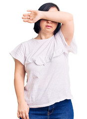 Sticker - Brunette woman with down syndrome wearing casual white tshirt covering eyes with arm, looking serious and sad. sightless, hiding and rejection concept