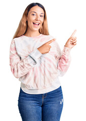 Canvas Print - Beautiful young woman wearing casual tie dye sweatshirt smiling and looking at the camera pointing with two hands and fingers to the side.