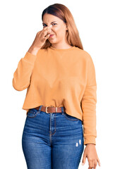 Sticker - Beautiful young woman wearing casual clothes smelling something stinky and disgusting, intolerable smell, holding breath with fingers on nose. bad smell