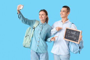 Poster - Students holding chalkboard with text SCHOOL GOODBYE and taking selfie on blue background. End of school concept