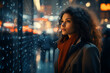 Thoughtful young woman with curly hair looking out rainy window at night city lights. Pensive mood, introspection and solitude in urban setting.