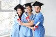 Medical graduate students with diplomas hugging in light room