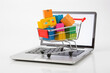 © twindesigner - Shopping cart full of vibrant boxes standing in front of laptop, white background. Ai generated