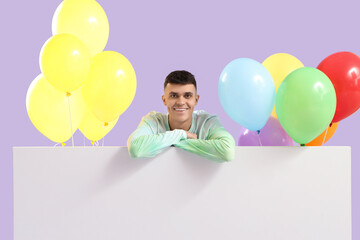 Sticker - Young man with bunches of colorful balloons and blank poster on lilac background