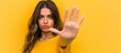 Young woman making stop gesture on yellow background