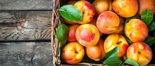   A Basket Brimming With Juicy Peaches Sits Beside Lush Green Foliage Atop A Wooden Table