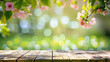 twigs with pink blossoms as spring frame in front of a green bokeh of a meadow and a wooden ground in warm bright look